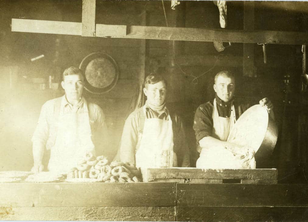 Three men (and a large pile of donuts) in the mess hall of an unidentified northwoods Wisconsin logging camp. Langlade County Historical Society.