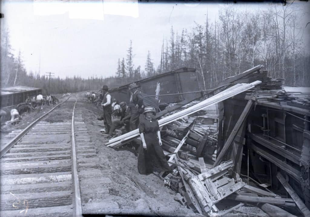 Overturned rail cars with passengers standing nearby. Glass negative by A. J. Kingsbury, 1900-1920. Langlade County Historical Society.