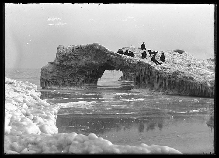 Several boys and a dog play on a massive ice formation on the shore of Lake Michigan, Kenosha County, February 1906. Photo by Louis Milton Thiers. Kenosha History Center.