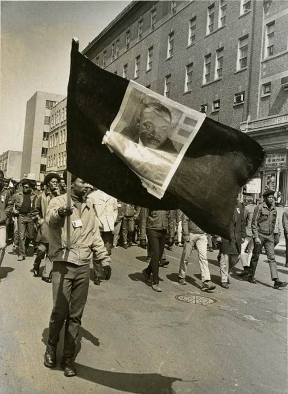 Man waves a flag with Dr. Martin Luther King, Jr.’s portrait on the first anniversary of King’s death, Milwaukee, 1969. Milwaukee Public Library.