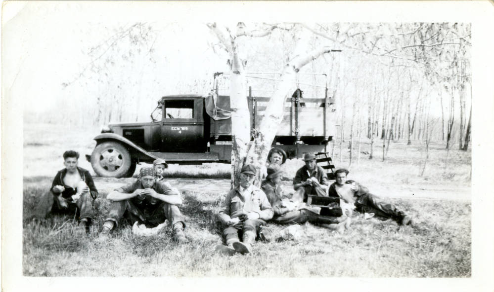 Lunch time in the field, CCC Camp 657, 1933-1937. Seven recruits and a forestry fire crew supervisor have a lunch break in the field sitting on the ground in front of the truck that delivered the lunches to them. 1933-1937. CCC Camp Elcho collection. 
Langlade County Historical Society.
