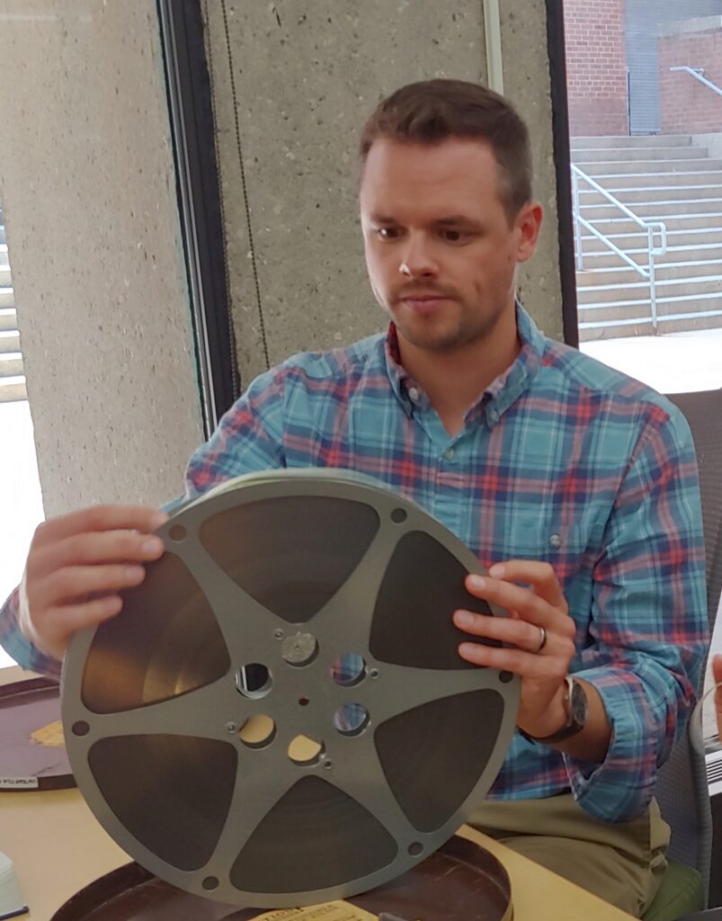 Dustin Mack sitting down looking at a film reel with neutral expression on his face