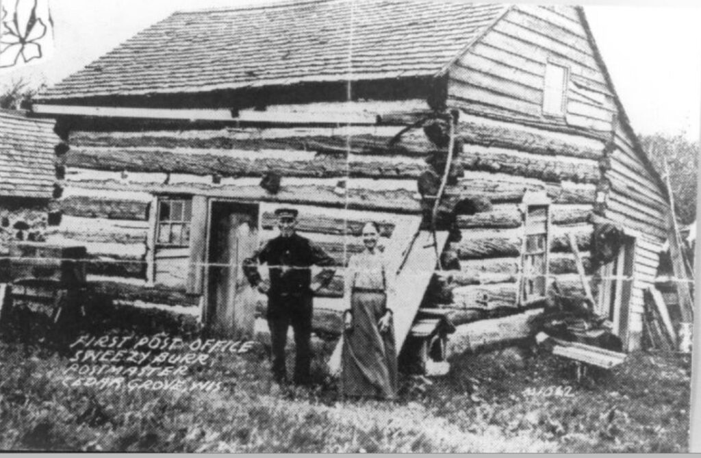 First Postmaster, Sweezy Burr, and his wife standing in front of the first Post Office, Cedar Grove, Wisconsin