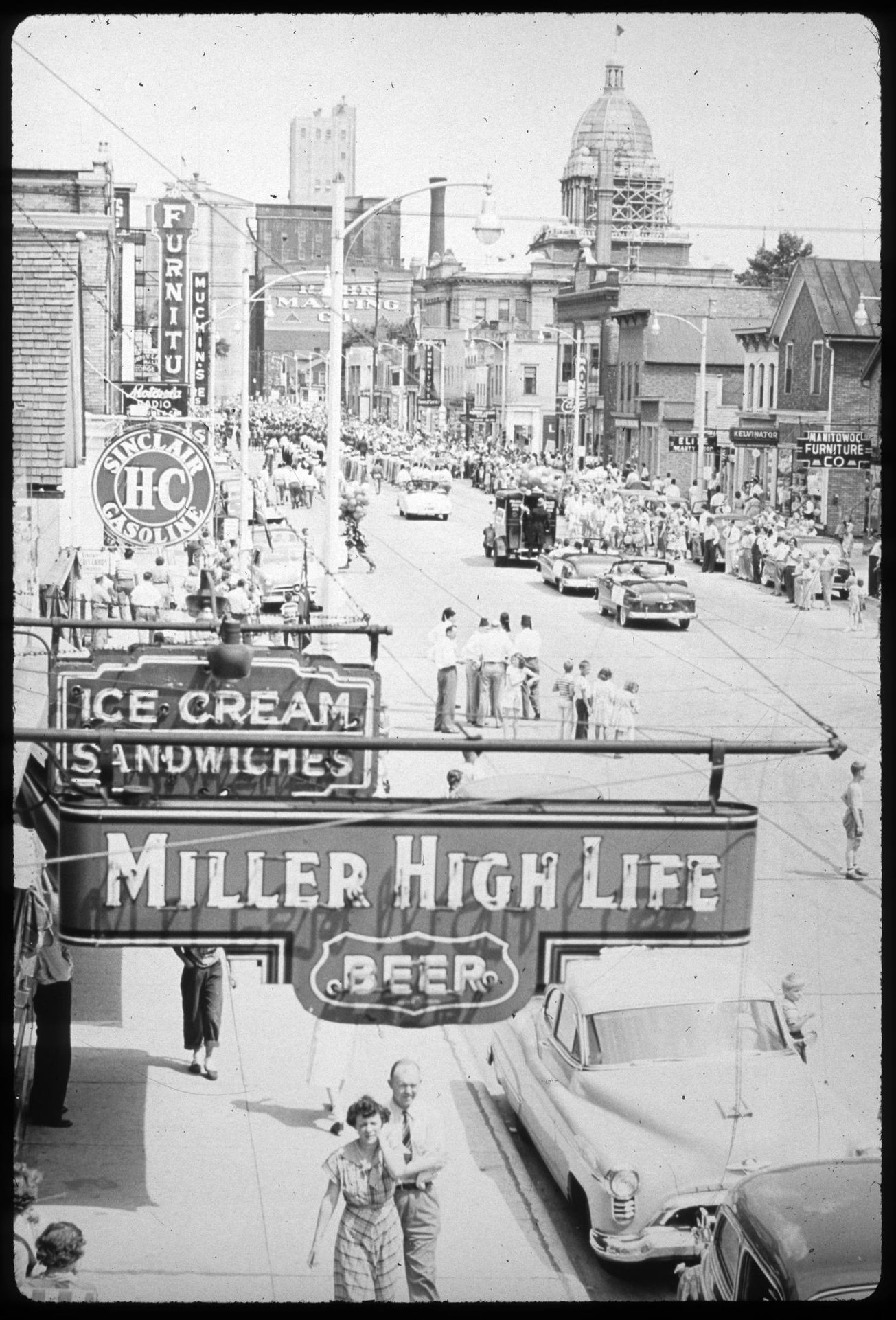 Taken from the upstairs of the Mikadow Theater looking east down Washington Street during a parade. Businesses in view include: Borris Furniture, Manitowoc Furniture Company, Siemers Refrigeration & Appliance Co., Elite Beauty Shop, Busse Radio Doctors, Inc, Rahr Malting, and the Manitowoc County Courthouse. Image taken by Francis Kadow. Undated.