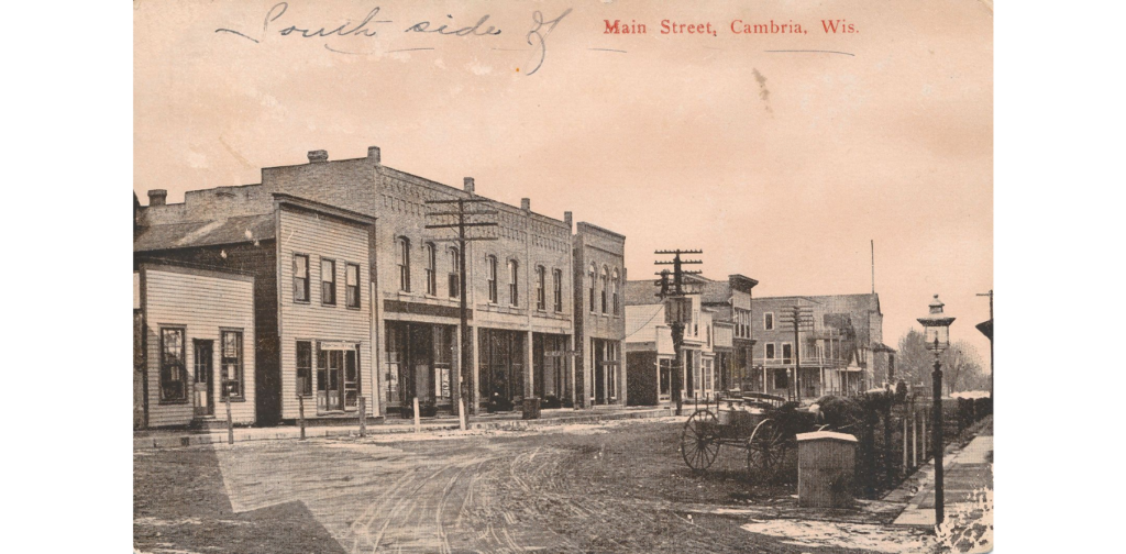 Main Street, Cambria, Wis. postcard 3, 1907. Street view showing main street buildings and gas street lamps.
