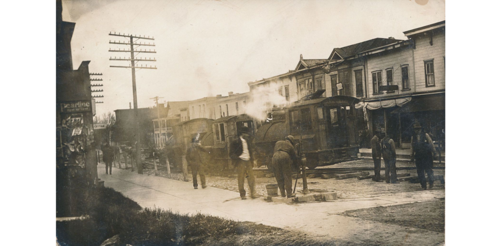 Building Northwestern Railroad postcard 1, 1910. Cambria main street with trucks carrying material for building the railway.