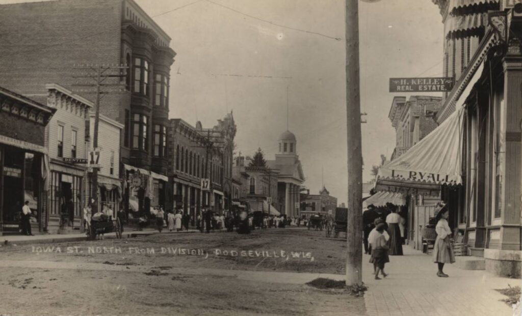 Northern Iowa Street with the buildings: Herman Heller Dry Goods, a dentist, Dodgeville Bank also known as the Reese Building, Iowa County Courthouse, Jones and Owens Building, The Auditorium, H. Kelley Real Estate, L. Ryall business, Strong's Bank ca. 1915.