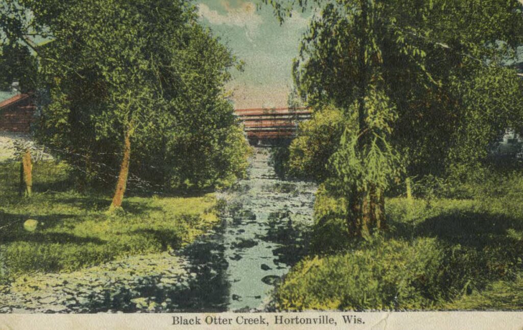 Postcard depicts Black Otter Creek and the bridge above it in Hortonville, Wis. The postcard is addressed to Mrs. Geo. Thern, New London, Wis., signed by Maggie. Postmark on back: Aug. 20, 1915, 6pm, Hortonville, Wis.