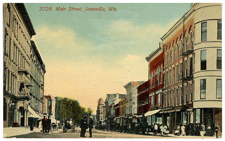 This color postcard shows Main Street from the north. The Courthouse which can be seen beyond the commercial buildings. Horses and buggies line the street and some pedestrians stand in the middle of the street, 1912.
