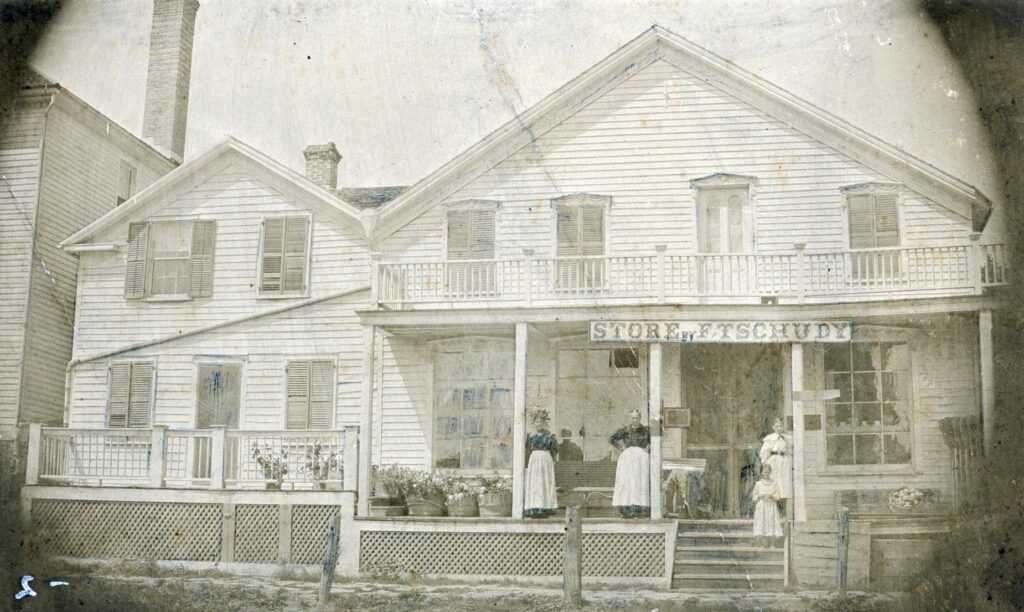 One of the first retail businesses in New Glarus, this store was built in 1866 by Fritz Tschudy. Standing in front of the store, left to right: Verena Tschudy Urban, Grandma Tschudy, Amelia Frick, and Molly Graf. This building, located in the 500 block of First Street, was later moved directly across the street, without turning the building, and became Kehrli's Cheese Store and Tavern.