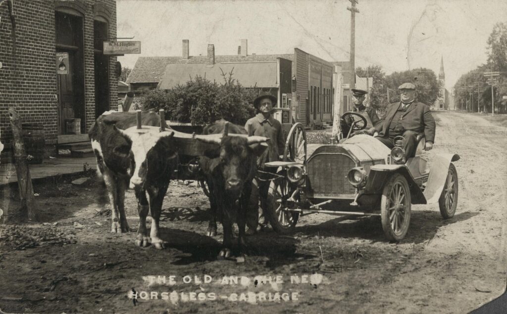 "The Old and the New." New Richmond resident Dr. Wade in his new automobile alongside unidentified man with yoked cattle, ca. 1908.