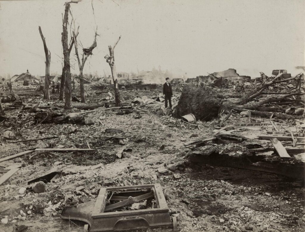 Young man stands amidst uprooted trees, debris and other rubble left in the wake of the June 12, 1899 tornado in New Richmond, Wisconsin.