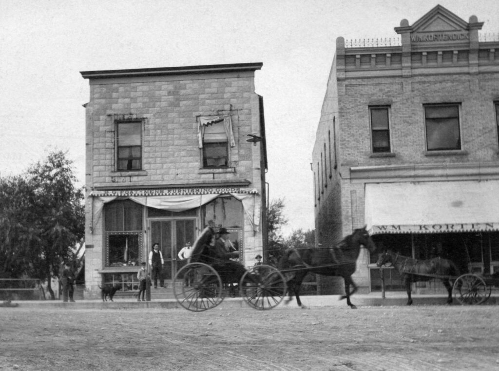 Foat Building - sporting goods store and barber shop, Kortendick meat market. Bert Foat on steps with an (unknown) boy, ca. 1890.