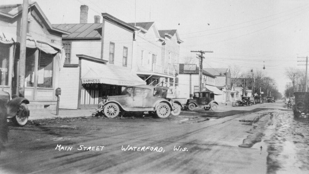 1930's view of Main Street, Waterford, Wisconsin. Waterford Post Office (USPS), Schenkenberg's Harness Shop, Town Tap, Howard Favell's Soda Fountain (upstairs), Pool Hall/Barbershop (downstairs) are shown.