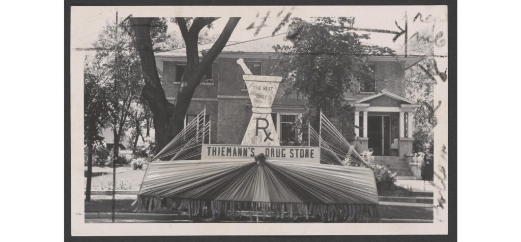 Thiemann's Drug Store parade float, undated. A parade float for Thiemann's Drug Store with a large mortar and pestle sits on a residential street. Caption reads: "This effective float was used by the Thiemann Drug Store of Reedsburg, Wis., in a July 4th parade."